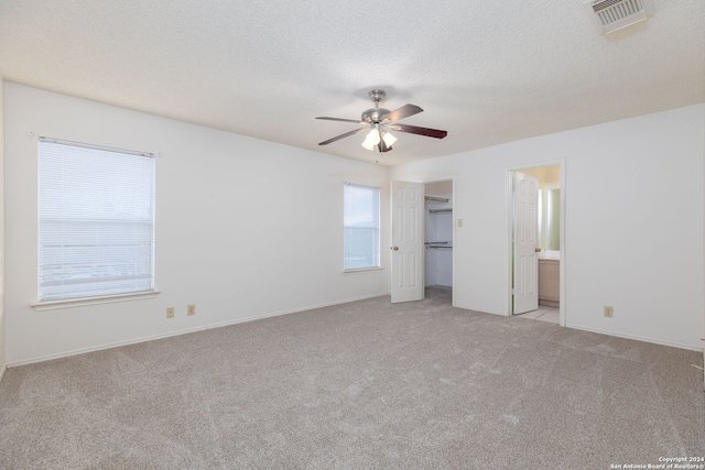 unfurnished bedroom with light carpet, a textured ceiling, connected bathroom, and ceiling fan