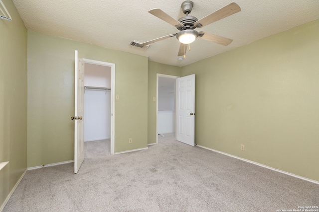 unfurnished bedroom featuring light carpet, ceiling fan, a spacious closet, a textured ceiling, and a closet