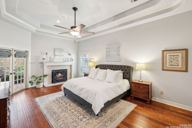 bedroom featuring ceiling fan, access to outside, dark hardwood / wood-style flooring, and a tray ceiling