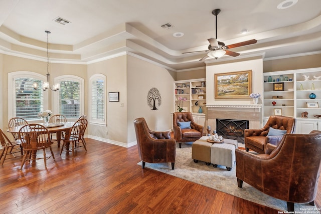 living room with hardwood / wood-style flooring, a premium fireplace, ceiling fan with notable chandelier, and a tray ceiling