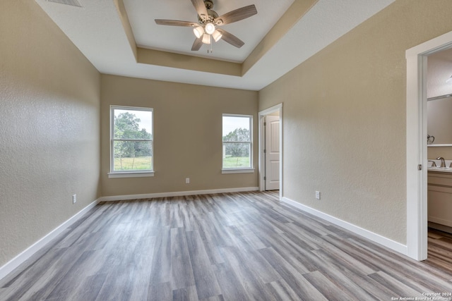 empty room with a tray ceiling, ceiling fan, a healthy amount of sunlight, and light wood-type flooring