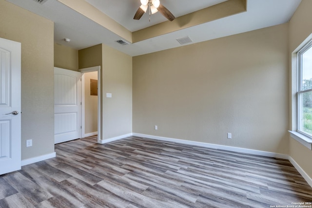 empty room with light wood-type flooring, a raised ceiling, and ceiling fan