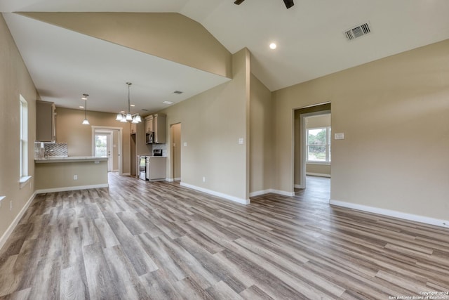 unfurnished living room with ceiling fan with notable chandelier, light hardwood / wood-style floors, and lofted ceiling