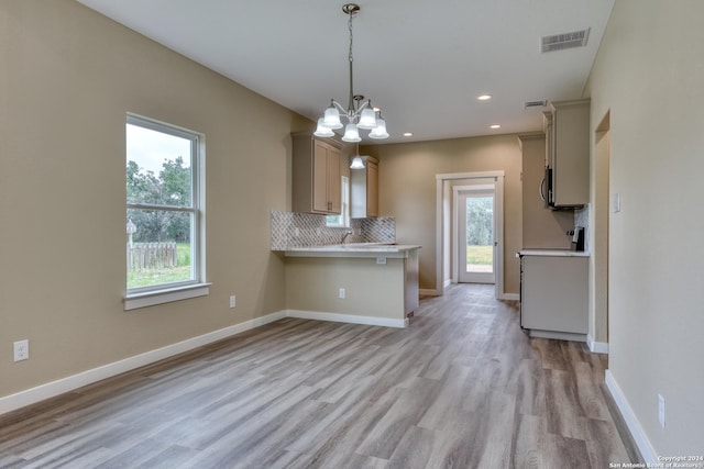 kitchen with pendant lighting, backsplash, a notable chandelier, light hardwood / wood-style floors, and kitchen peninsula