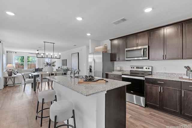 kitchen featuring light stone countertops, sink, stainless steel appliances, light hardwood / wood-style flooring, and a center island with sink