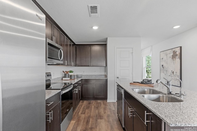 kitchen with light stone countertops, appliances with stainless steel finishes, dark hardwood / wood-style flooring, dark brown cabinets, and sink