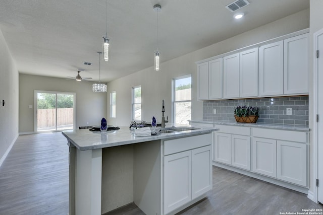 kitchen with ceiling fan, hanging light fixtures, an island with sink, white cabinets, and light wood-type flooring