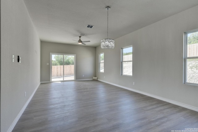 spare room with ceiling fan with notable chandelier, dark wood-type flooring, and a healthy amount of sunlight