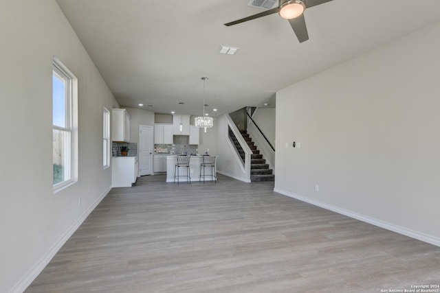 unfurnished living room with light hardwood / wood-style flooring and ceiling fan with notable chandelier