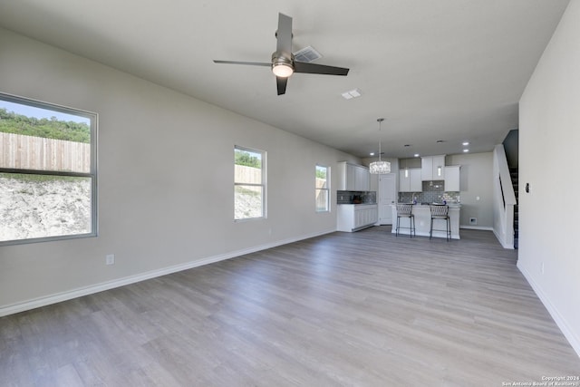 unfurnished living room with ceiling fan with notable chandelier, a healthy amount of sunlight, and light wood-type flooring