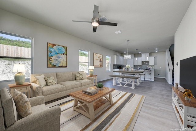 living room featuring ceiling fan with notable chandelier, a healthy amount of sunlight, and light hardwood / wood-style floors