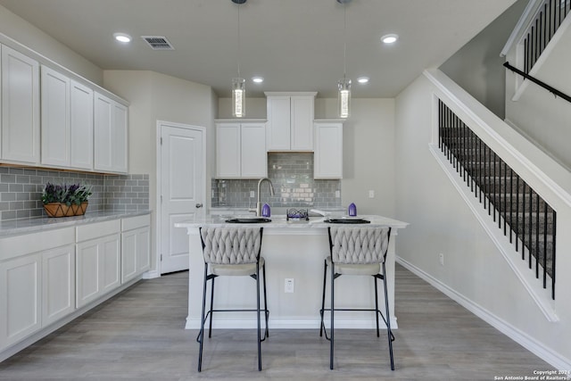 kitchen featuring decorative light fixtures, light wood-type flooring, white cabinetry, and a kitchen island with sink