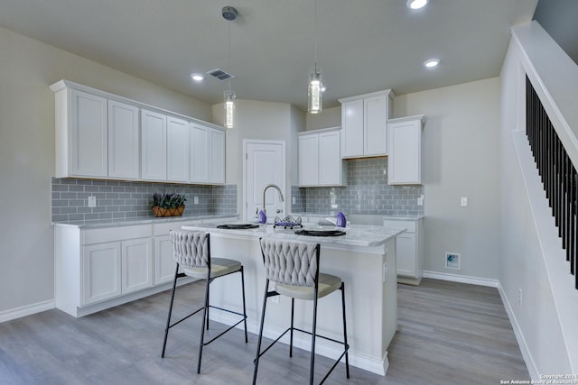 kitchen with white cabinetry, tasteful backsplash, light hardwood / wood-style floors, decorative light fixtures, and a center island with sink