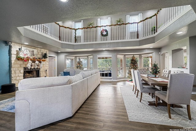 living room with a stone fireplace, dark hardwood / wood-style flooring, a towering ceiling, and a textured ceiling