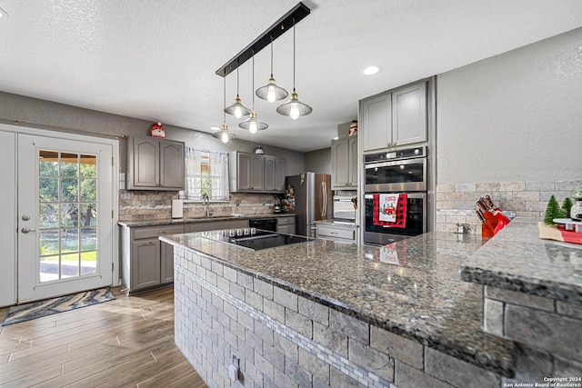 kitchen with kitchen peninsula, tasteful backsplash, dark wood-type flooring, black appliances, and hanging light fixtures