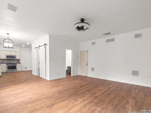 unfurnished living room featuring a barn door, an inviting chandelier, light hardwood / wood-style flooring, and crown molding