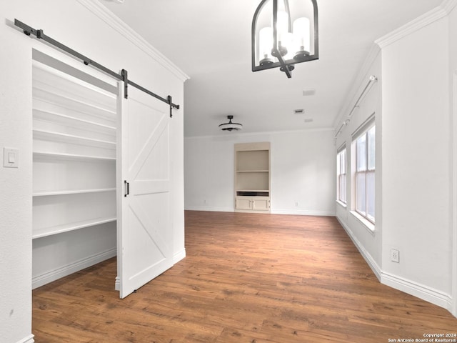 unfurnished living room featuring a chandelier, a barn door, dark hardwood / wood-style floors, and ornamental molding