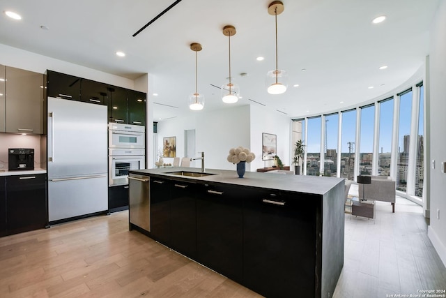 kitchen featuring a center island with sink, sink, hanging light fixtures, fridge, and light hardwood / wood-style floors