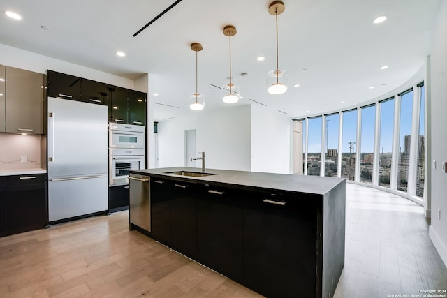 kitchen featuring refrigerator, double oven, a kitchen island with sink, sink, and decorative light fixtures