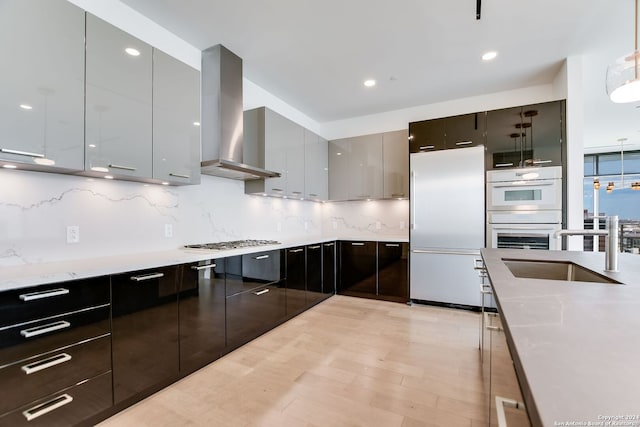 kitchen with decorative backsplash, white appliances, hanging light fixtures, and wall chimney range hood