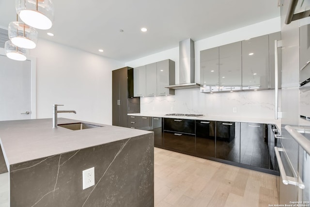 kitchen featuring gray cabinetry, sink, wall chimney range hood, light hardwood / wood-style flooring, and pendant lighting