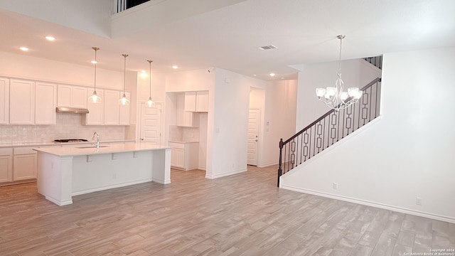 kitchen featuring backsplash, light wood-type flooring, a kitchen island with sink, and hanging light fixtures