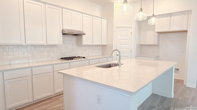 kitchen with white cabinets, decorative light fixtures, sink, and an island with sink