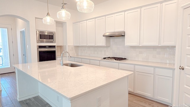 kitchen with white cabinetry, sink, hanging light fixtures, stainless steel appliances, and a center island with sink