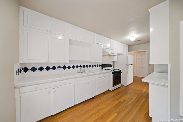 kitchen with white range with gas stovetop, light wood-type flooring, tile countertops, and white cabinetry