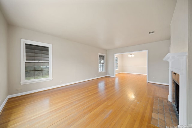 unfurnished living room with a chandelier, light wood-type flooring, and a brick fireplace