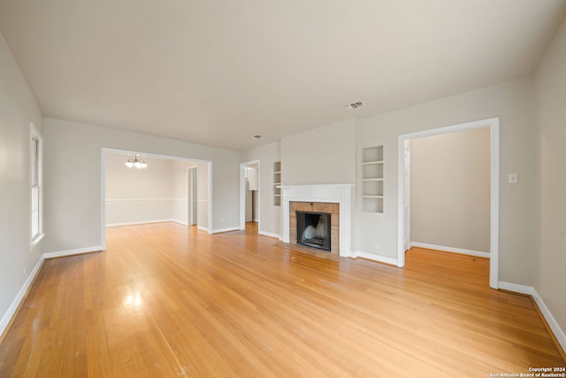 unfurnished living room with a brick fireplace, built in features, light hardwood / wood-style floors, and an inviting chandelier