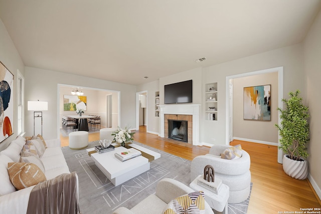 living room with a tile fireplace, hardwood / wood-style floors, built in shelves, and an inviting chandelier