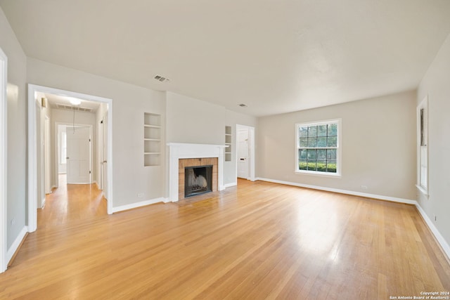 unfurnished living room with built in shelves, light hardwood / wood-style flooring, and a tiled fireplace