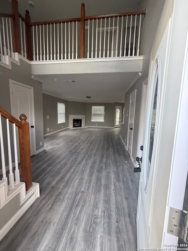 unfurnished living room featuring dark hardwood / wood-style flooring, a towering ceiling, and ornamental molding