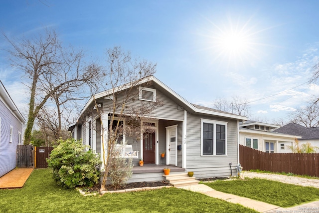 bungalow-style house featuring covered porch, fence, and a front lawn