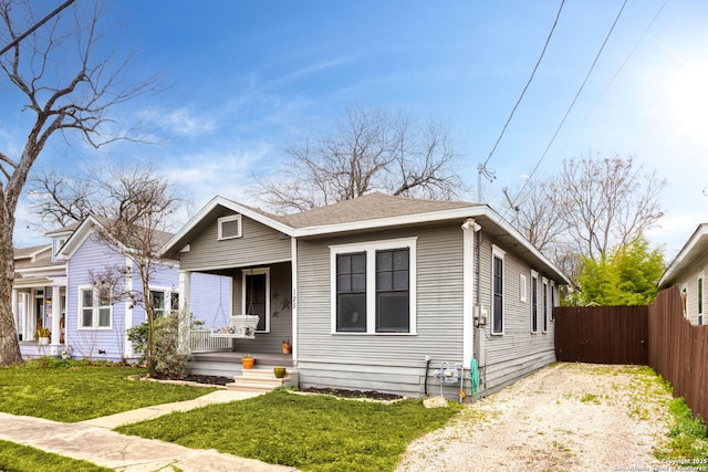 bungalow-style home featuring a porch, a shingled roof, fence, a front lawn, and gravel driveway