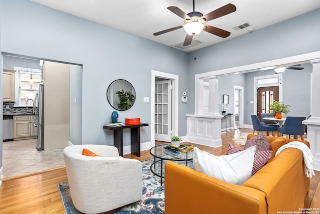 living area featuring light wood-type flooring, decorative columns, visible vents, and a ceiling fan