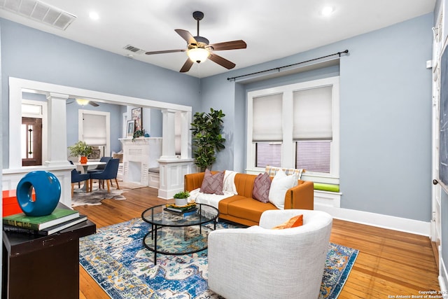 living area featuring a ceiling fan, visible vents, decorative columns, and wood finished floors