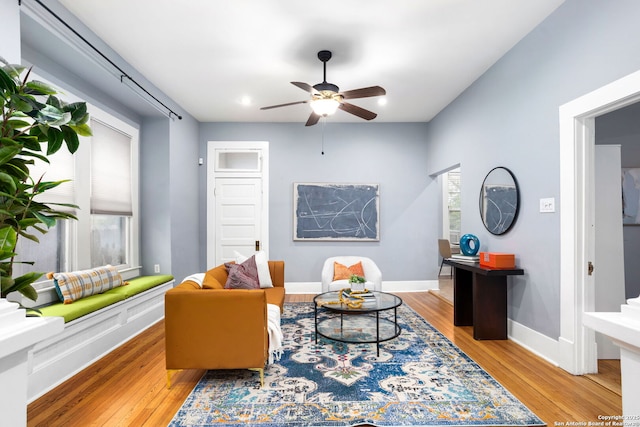 living area featuring light wood finished floors, a ceiling fan, and baseboards