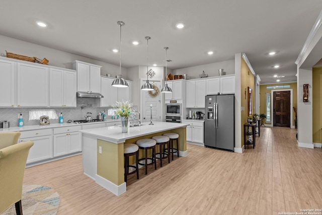 kitchen featuring appliances with stainless steel finishes, an island with sink, a kitchen bar, white cabinetry, and decorative light fixtures