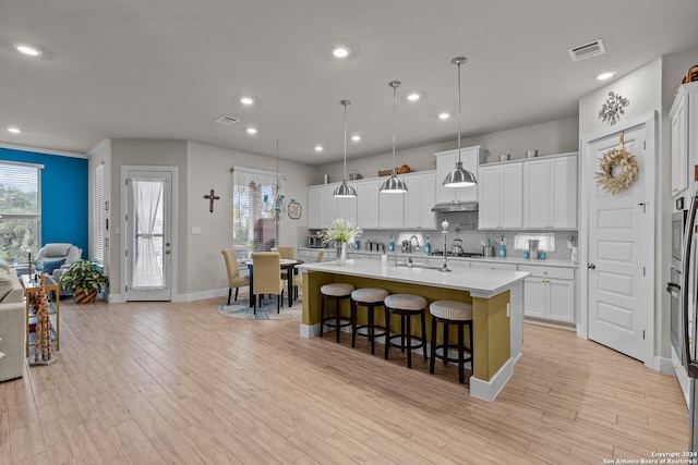 kitchen with a kitchen breakfast bar, a kitchen island with sink, pendant lighting, and white cabinetry