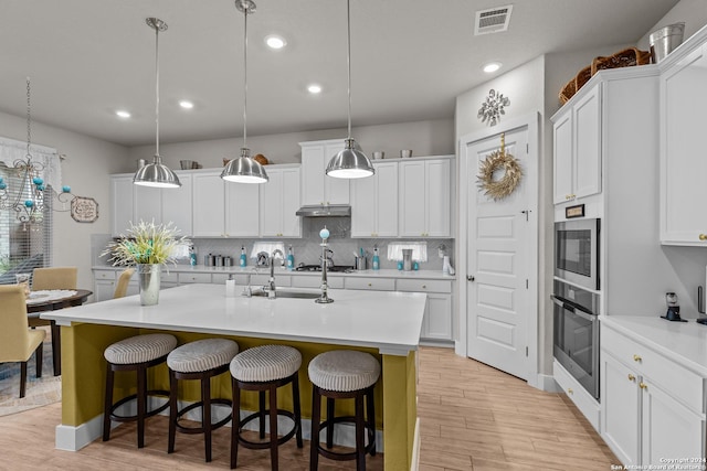 kitchen featuring stainless steel appliances, a center island with sink, white cabinetry, and hanging light fixtures