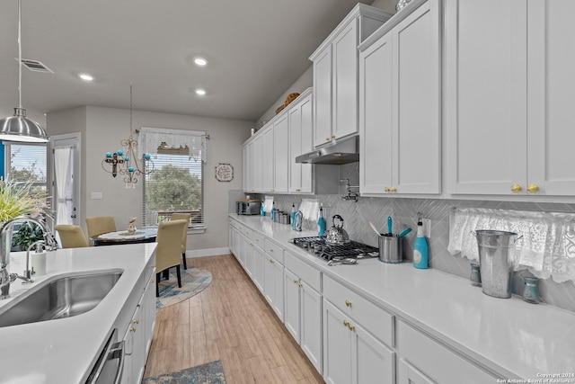 kitchen with hanging light fixtures, tasteful backsplash, stainless steel gas cooktop, white cabinets, and sink