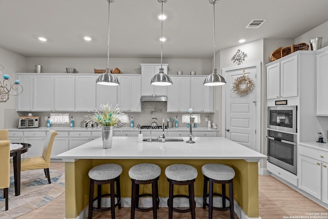 kitchen with white cabinets, a center island with sink, and pendant lighting