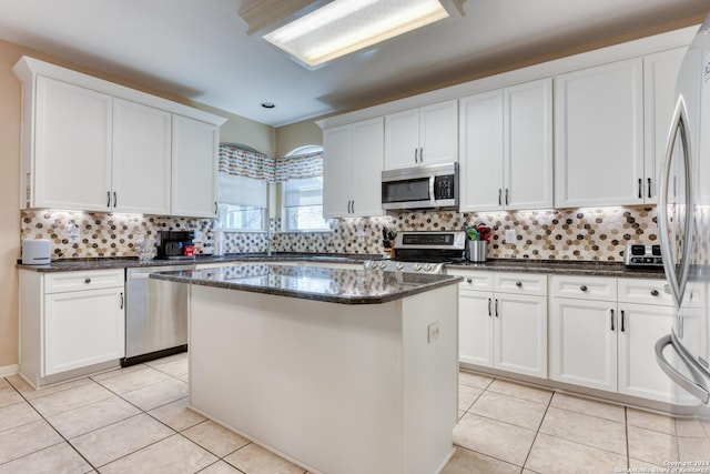 kitchen with stainless steel appliances, light tile patterned floors, a kitchen island, and white cabinets