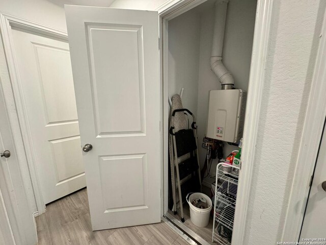 clothes washing area with light hardwood / wood-style floors and tankless water heater