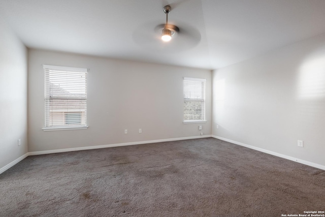 unfurnished room featuring dark colored carpet, plenty of natural light, and ceiling fan