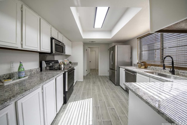 kitchen with a raised ceiling, sink, white cabinetry, and stainless steel appliances