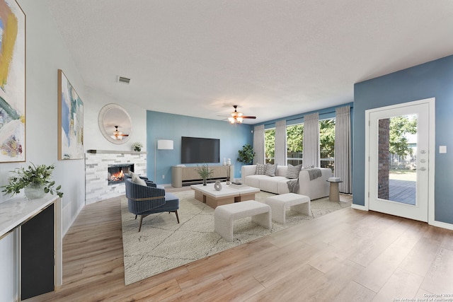 living room with ceiling fan, light wood-type flooring, a textured ceiling, and a tile fireplace