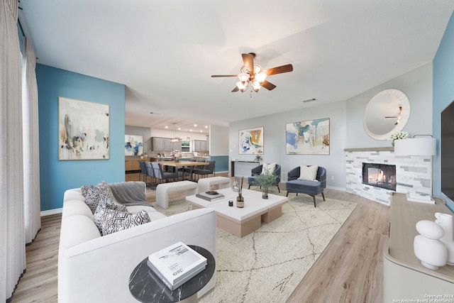 living room featuring a tiled fireplace, ceiling fan, and light hardwood / wood-style floors